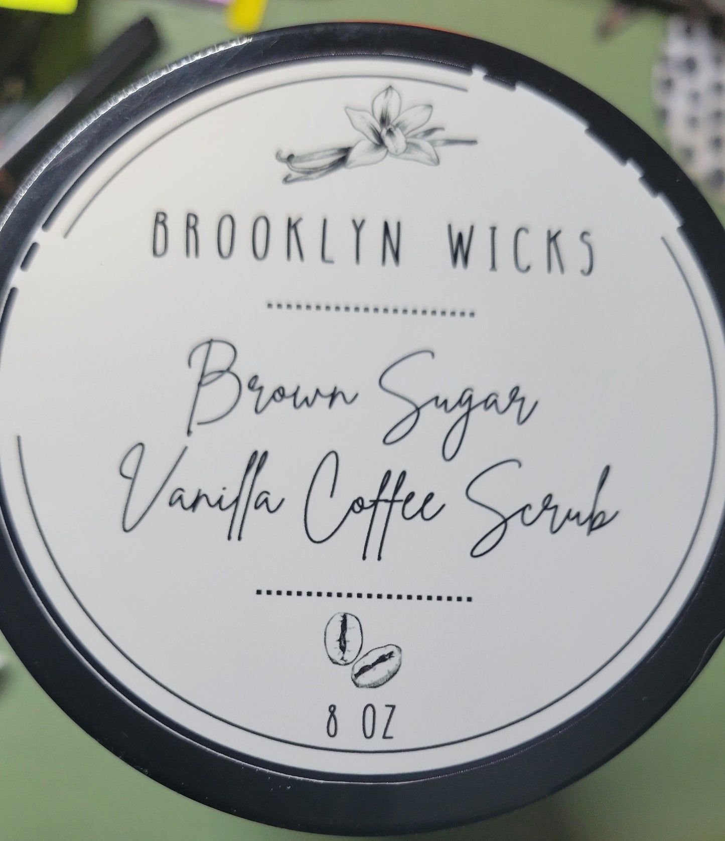 Jar of brown sugar vanilla coffee body scrub with visible texture, surrounded by natural ingredients like coffee beans and vanilla pods.